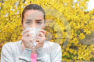 Young woman with nose wiper near blooming tree. Allergy concept