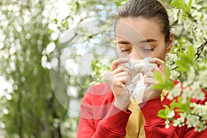 Young woman with nose wiper near blooming tree. Allergy concept