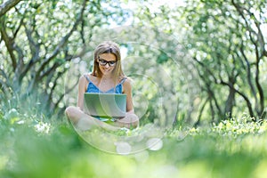 Young woman with notebook in park looking at notebook computer