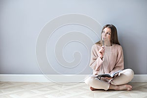 Young woman with notepad think hard sitting on a wooden floor