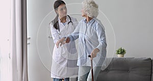 Young woman nurse caregiver help senior grandmother hold cane stick