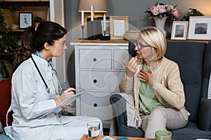 Young woman nurse doctor gp holding stethoscope examining old senior 60s grandma patient check heartbeat at homecare checkup