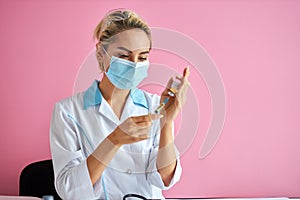 Young woman nurse in protective suit and mask holds an injection syringe and vaccine