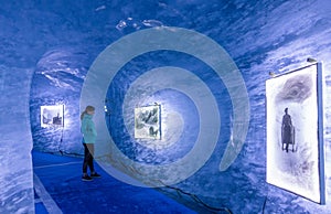 Young woman observes the photos inside of a blue ice cave in the French Alps.