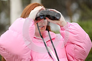 Young woman observes the trees with black binoculars