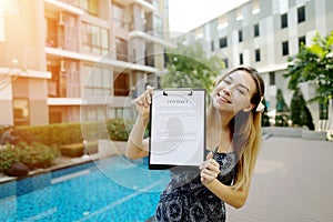 Young woman offer to sign contract document on background of new apartment building. Front used with Open Font License