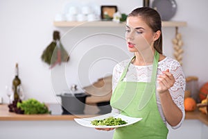 Young woman is offering fresh salad while cooking in a kitchen