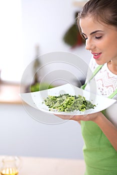 Young woman is offering fresh salad while cooking in a kitchen