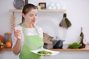 Young woman is offering fresh salad while cooking in a kitchen