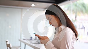 Young woman office worker using mobile phone while standing in office.