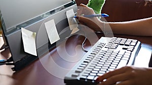 Young woman in office writing on sticker stuck on monitor