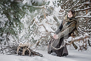 Young woman in old clothes sitting with brushwood in winter forest. character from the fairy tale