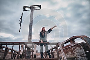 A young woman in old clothes stands on Board an old pirate ship. Girl the Corsair shows up where there is land