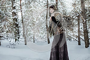 A young woman in old clothes stands with brushwood in a winter forest. character from the fairy tale