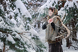 A young woman in old clothes stands with brushwood in a winter forest. character from the fairy tale