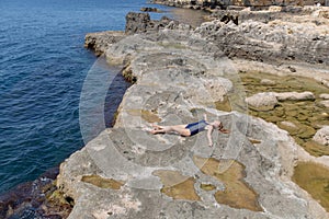 Young woman in one-piece swimsuit resting on rocky seashore