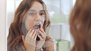 Young woman with opened mouth checking teeth in mirror in home bath room