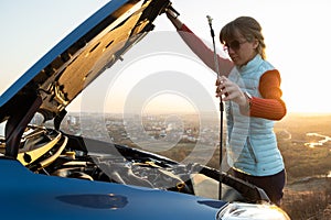 Young woman opening bonnet of broken down car having trouble with her vehicle. Female driver near auto with popped up hood