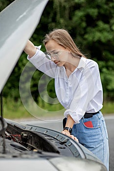 Young woman opening bonnet of broken down car having trouble with her vehicle. Worried woman talking on the phone near broken car