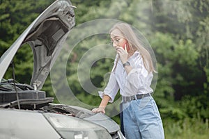 Young woman opening bonnet of broken down car having trouble with her vehicle. Worried woman talking on the phone near broken car