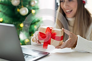 Young woman opening Christmas or new year present when calling to friends via video chat from home