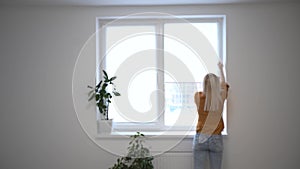 Young woman opening curtain looking through window. Happy confident lady enjoying beautiful view and dreaming at home