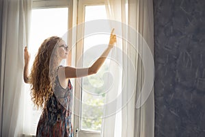 Young woman opening the curtain in the morning