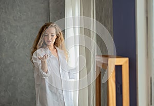 Young woman opening the curtain in the morning