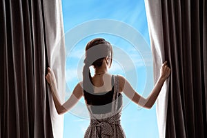 Young woman opening curtains and blue sky