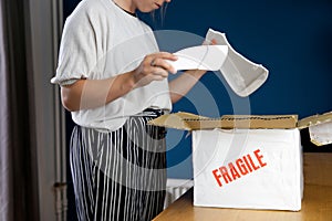 Young woman opening damaged delivery package,online shopping package. Broken fragile plate at home