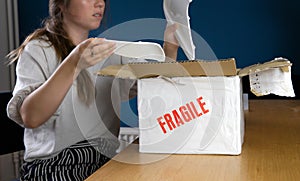 Young woman opening damaged delivery package,online shopping package. Broken fragile plate at home