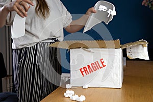 Young woman opening damaged delivery package,online shopping package. Broken fragile plate at home