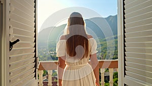 Young woman opening her window blinds and enjoying the mountain sunrise or sunset. Vacation and nature& x27;s beauty.