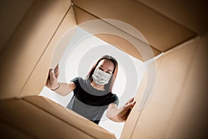 Young woman opening the huge postal package wearing protective face mask, contactless delivery