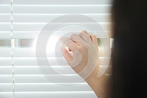 Young woman opening window blinds, closeup.