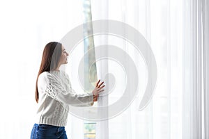 Young woman opening window curtains