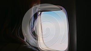 A young woman opens an airplane window and looks out the window. The dark frame is illuminated with the opening of the