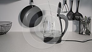 young woman opens a jar of glass electric kettle and pours cool water for boiling on kitchen table background of