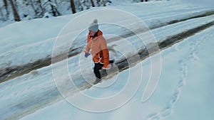 Young woman in orange jacket runs with gray puppy of Husky breed in winter forest and on snowy road