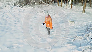 Young woman in orange jacket runs with gray puppy of Husky breed in winter forest and on snowy road