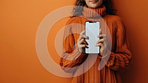 Young Woman in Orange Sweater Holding Smartphone on Vivid Orange Background