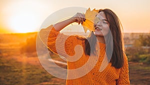 Young woman in a orange sweater with with yellow leaves, outdoor portrait in soft sunny daylight. Autumn. Sunset. Cozy