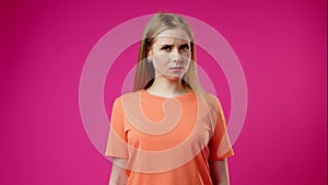 Young Woman in Orange T-Shirt Expressing Confusion Against Vivid Pink Background