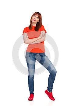 Young Woman In Orange T-Shirt, Jeans And Red Sneakers Is Standing, Looking Away And Thinking