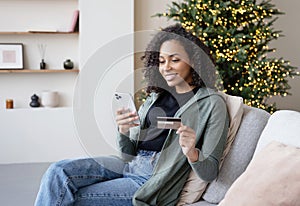 Young woman ordering gift during Christmas holiday at home using smartphone and credit card. Shopping online during holidays