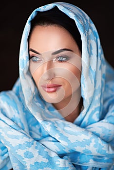Young woman of oriental appearance in a blue scarf. Beauty portrait of arabian or indian girl with perfect makeup