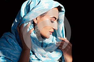 Young woman of oriental appearance in a blue scarf. Beauty portrait of arabian or indian girl with perfect makeup