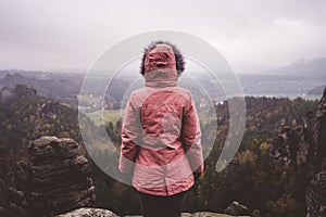 Young woman in outdoor clothing standing alone on mountain top with wild forest in the valley in background. Travel