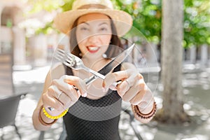 Young woman in outdoor restaurant with a knife and fork in her hands