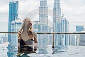 Young woman in outdoor swimming pool with city view in blue sky